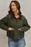 Woman wearing a green jacket with a brown collar against a neutral background