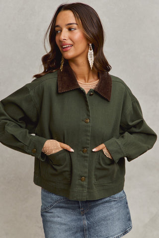 Woman wearing a green jacket with a brown collar against a neutral background