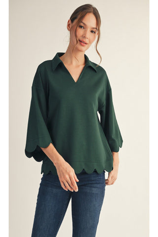 Woman wearing a green blouse with scalloped hem on a beige background