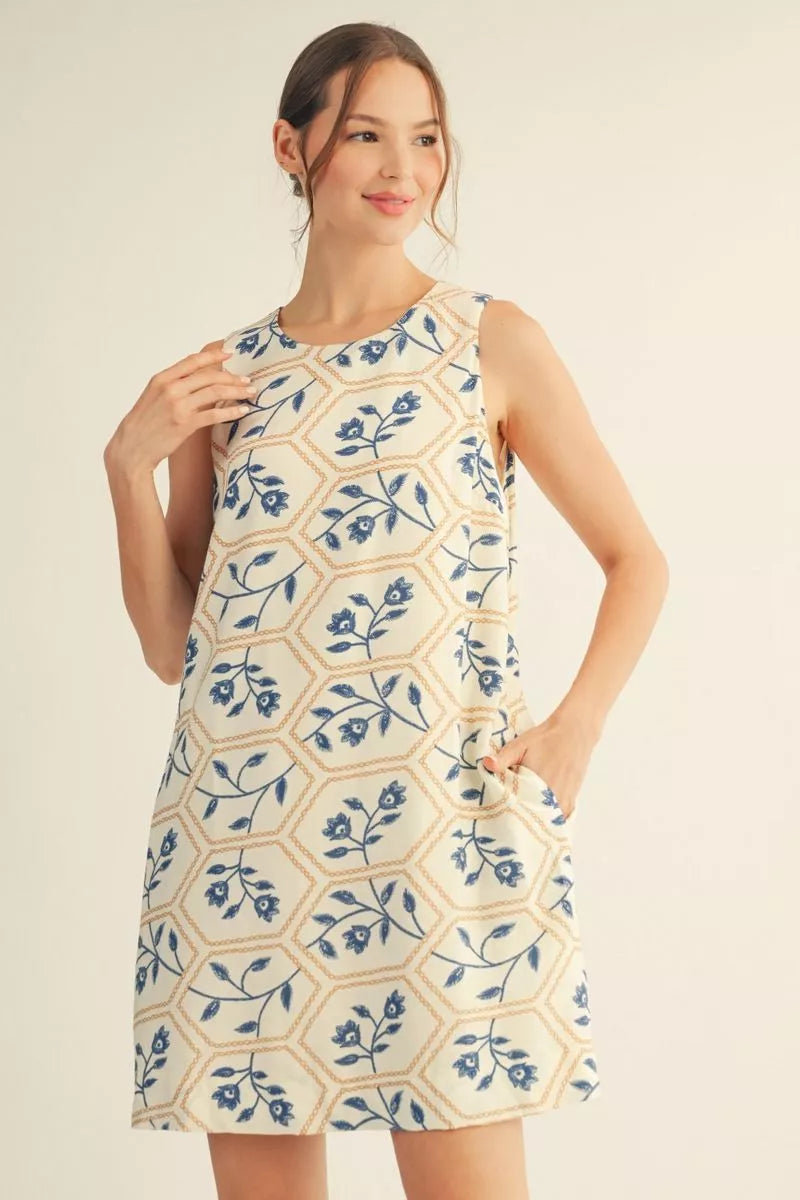 Woman wearing a sleeveless dress with blue floral pattern on a beige background