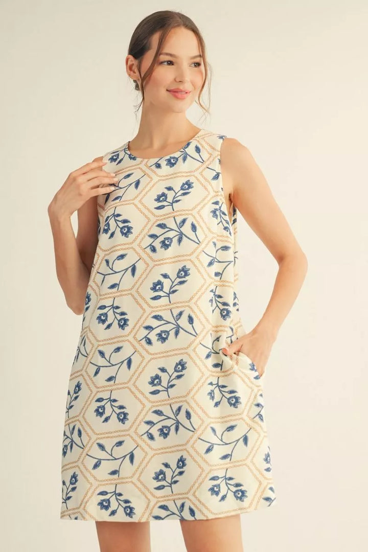 Woman wearing a sleeveless dress with blue floral pattern on a beige background