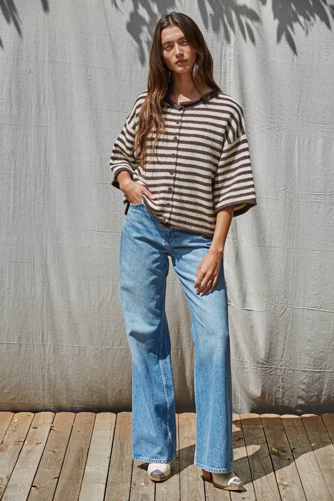 Woman wearing a striped sweater and blue jeans standing against a textured wall.