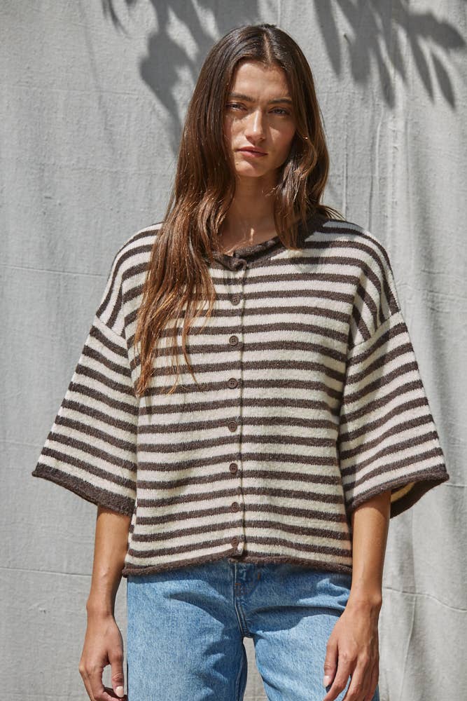 Woman wearing a striped shirt and blue jeans against a textured wall.