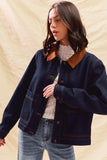 Woman wearing a dark denim jacket over a white sweater with a beige background