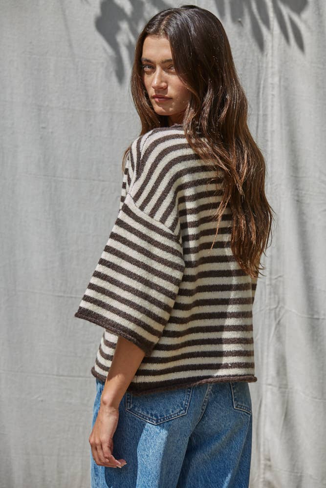 Woman wearing a striped sweater and jeans against a textured wall.