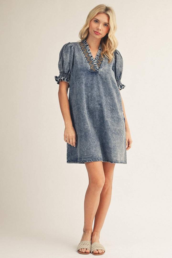 Woman wearing a denim dress with lace trim on a plain background