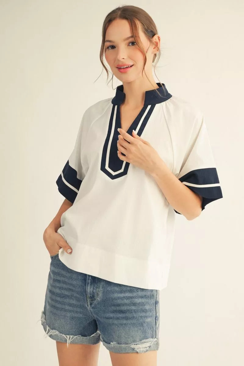 Woman wearing a white shirt with navy accents and denim shorts on a plain background