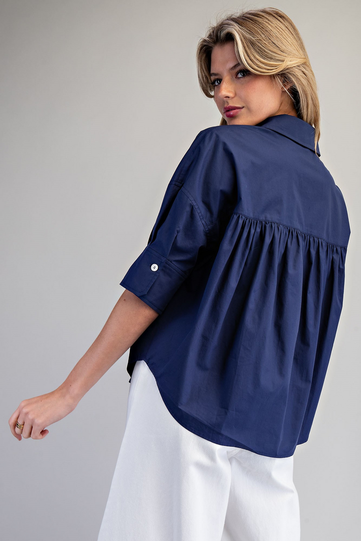 Woman wearing a navy blue blouse with rolled-up sleeves on a gray background