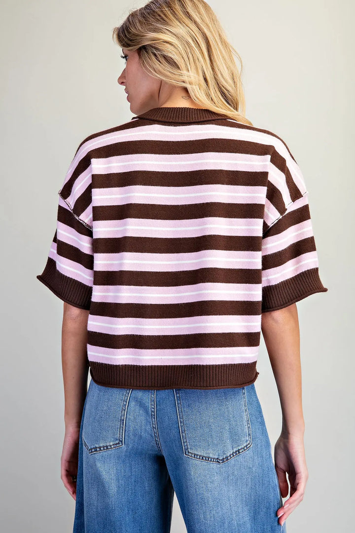 A woman shown from the back wearing a brown and light pink striped short-sleeve knit top with blue jeans, against a plain light gray studio background.