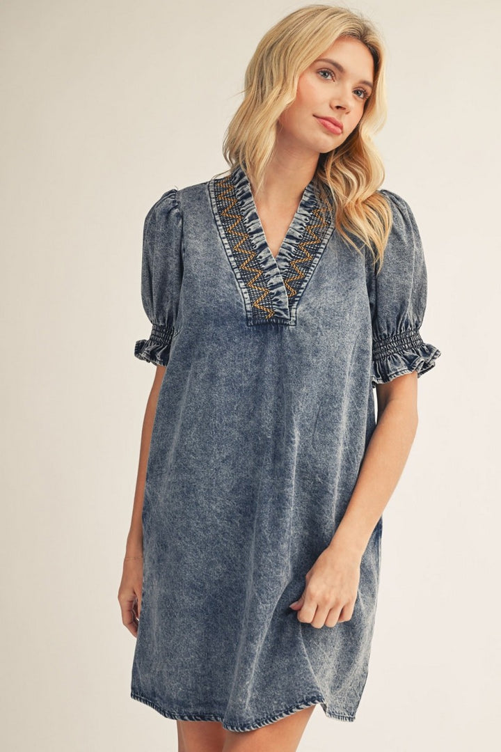 Woman wearing a denim dress with embroidered details on a plain background