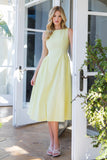 Woman in a light yellow dress standing in front of a white door with glass panels.