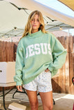 Person wearing a light green sweatshirt with 'JESUS' printed on it, standing outdoors.