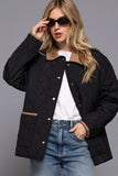 Woman wearing a black quilted jacket, white shirt, and blue jeans against a gray background