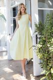 Woman in a light yellow dress standing outdoors near a white door.