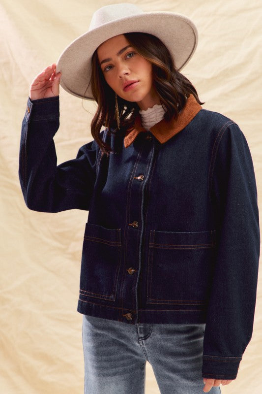 Person wearing a navy denim jacket, light blue jeans, and a white hat on a beige background