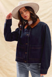 Person wearing a navy denim jacket, light blue jeans, and a white hat on a beige background