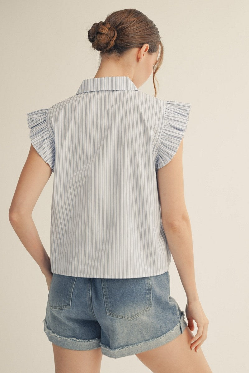 Woman wearing a sleeveless striped shirt with ruffled shoulders and denim shorts on a beige background