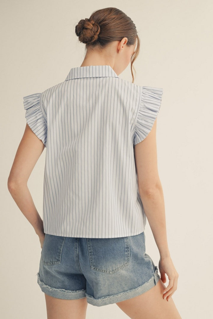 Woman wearing a sleeveless striped shirt with ruffled shoulders and denim shorts on a beige background