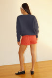 Person wearing a navy sweater and red shorts standing against a plain wall.