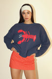 Woman wearing a navy sweater with a red lobster design and a red and white striped skirt on a beige background