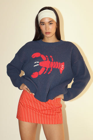 Woman wearing a navy sweater with a red lobster design and a red and white striped skirt on a beige background