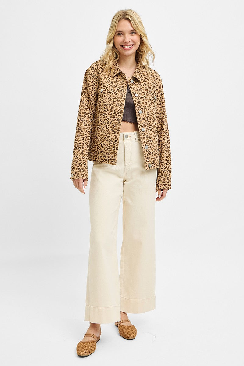 Woman wearing a leopard print jacket, black top, beige pants, and brown shoes on a white background