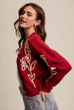 Woman wearing a red sweater with floral embroidery on a beige background