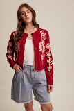 Woman wearing a red embroidered cardigan with denim shorts on a beige background