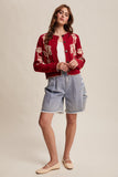 Woman wearing a red embroidered cardigan with denim shorts on a beige background