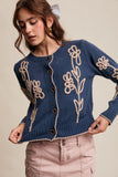Woman wearing a blue cardigan with floral embroidery on a beige background