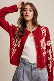 Woman wearing a red cardigan with floral embroidery on a beige background