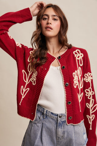 Woman wearing a red cardigan with floral embroidery on a beige background