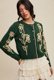 Woman wearing a green cardigan with floral embroidery on a beige background