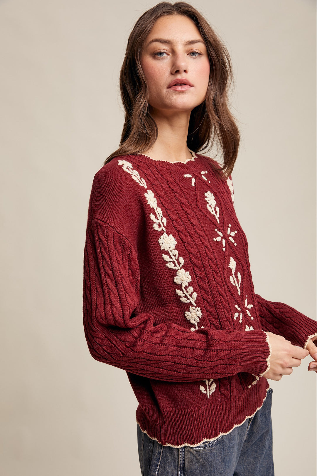 Woman wearing a burgundy sweater with floral embroidery on a beige background