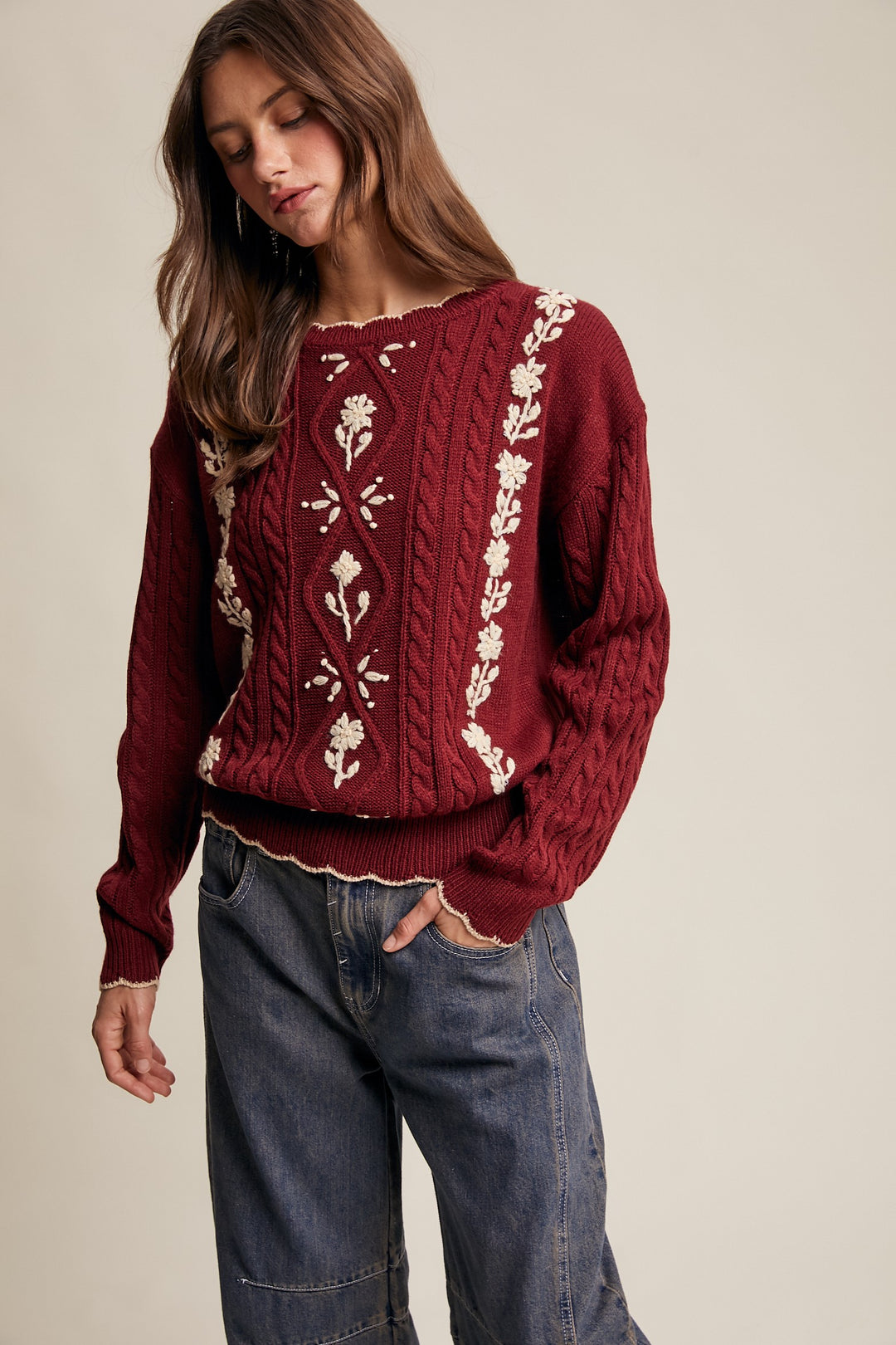 Woman wearing a burgundy sweater with floral patterns on a beige background