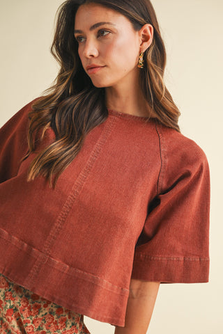 Woman wearing a rust-colored top with a neutral background
