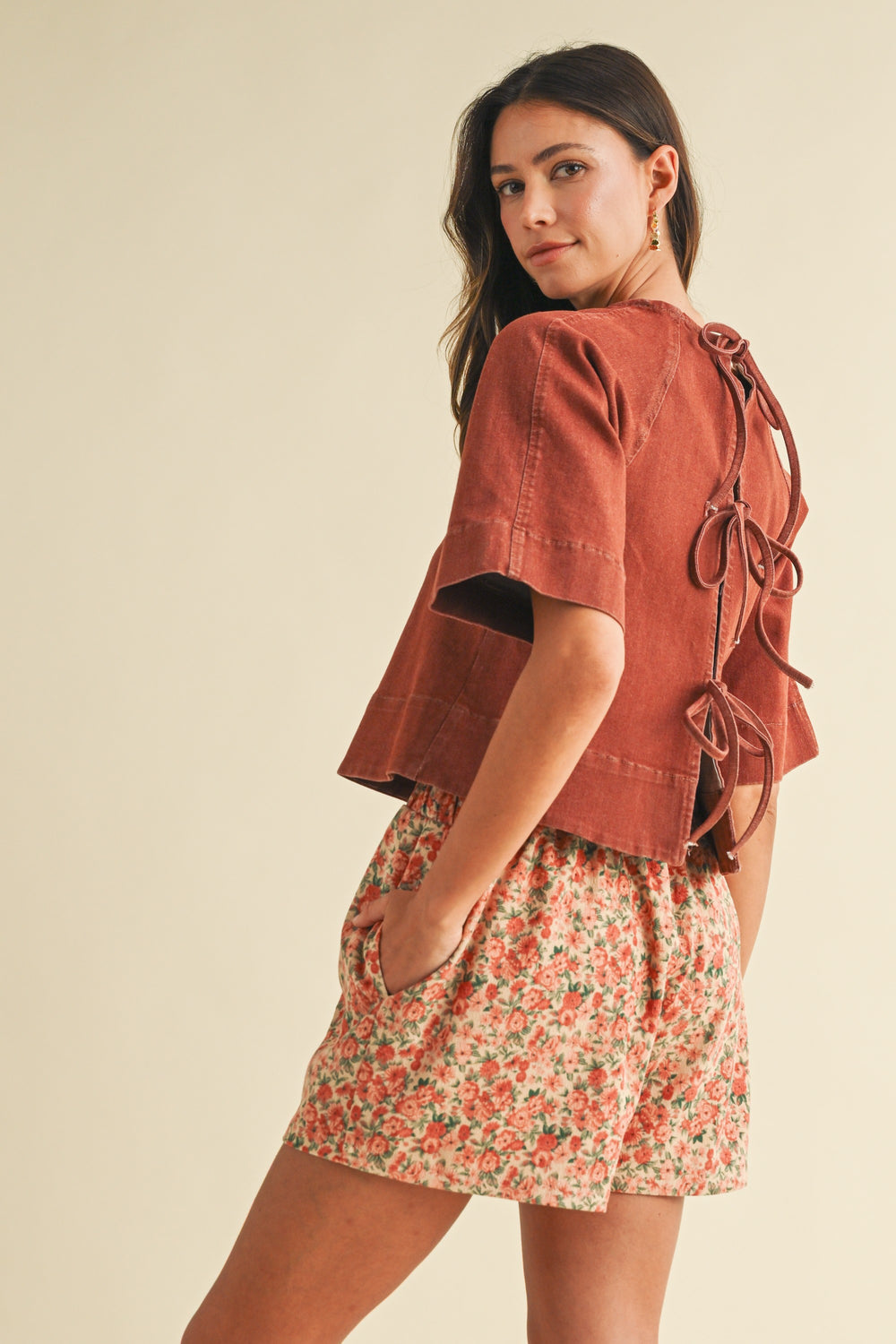 Woman wearing a rust-colored top and floral skirt on a beige background