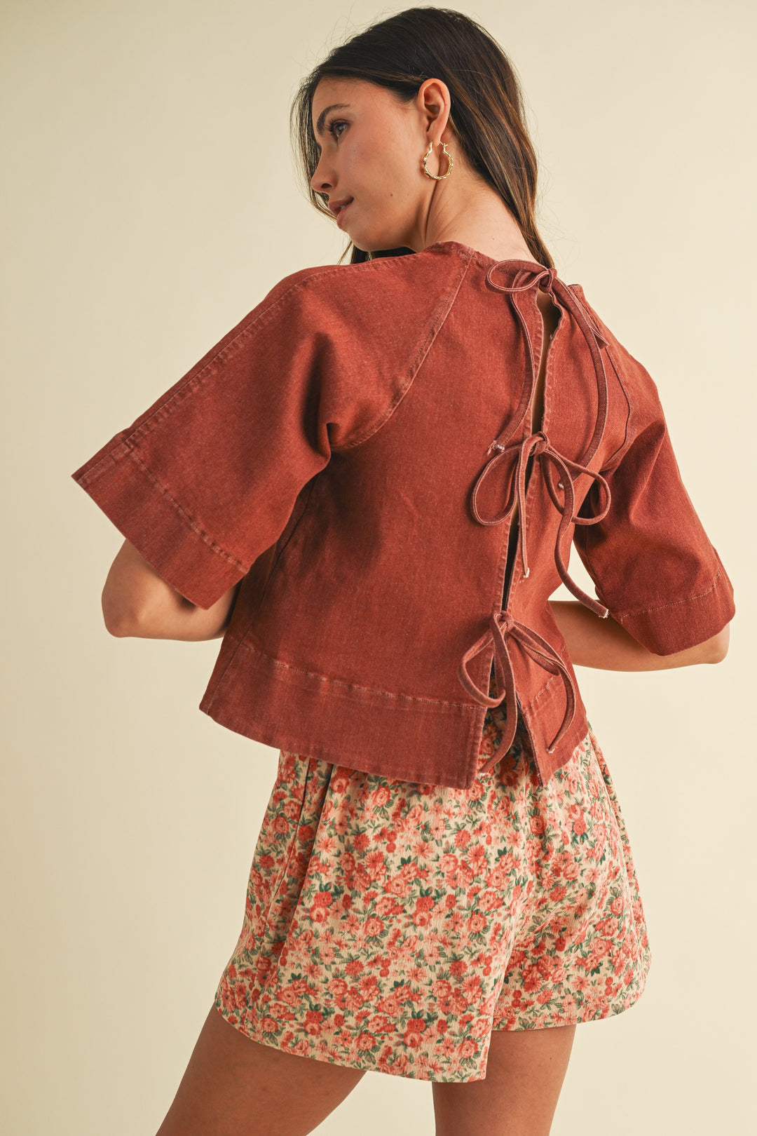 Woman wearing a rust-colored jacket and floral skirt on a beige background