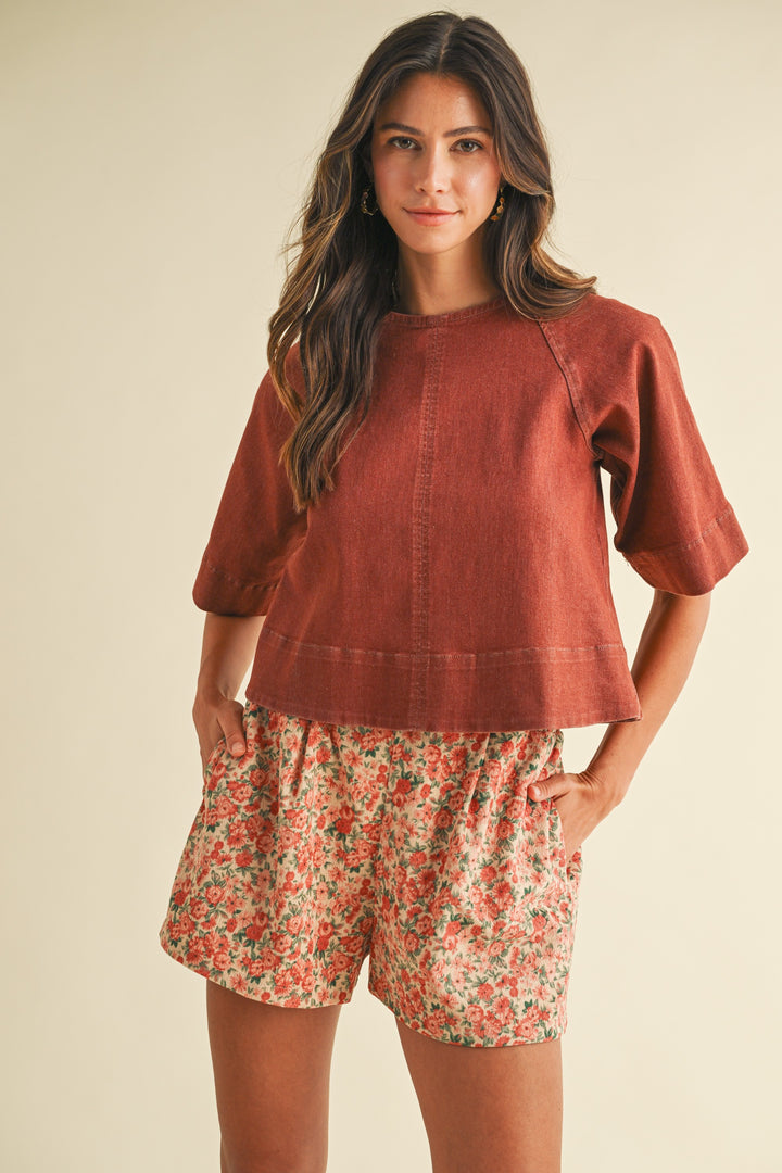 Woman wearing a rust-colored top and floral shorts on a beige background