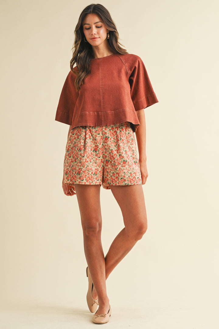 Woman wearing a rust-colored top and floral shorts on a beige background