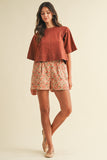 Woman wearing a rust-colored top and floral shorts on a beige background