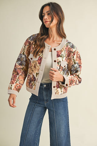 Woman wearing a floral bomber jacket and blue jeans on a beige background