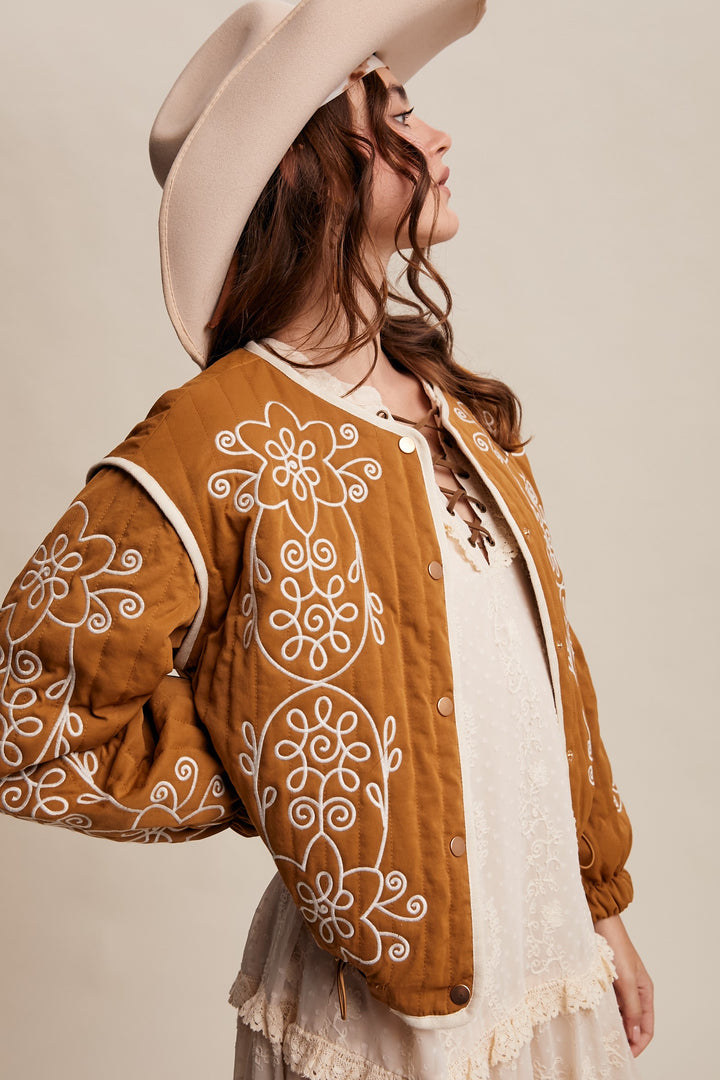 Woman wearing a brown embroidered jacket and beige hat against a beige background
