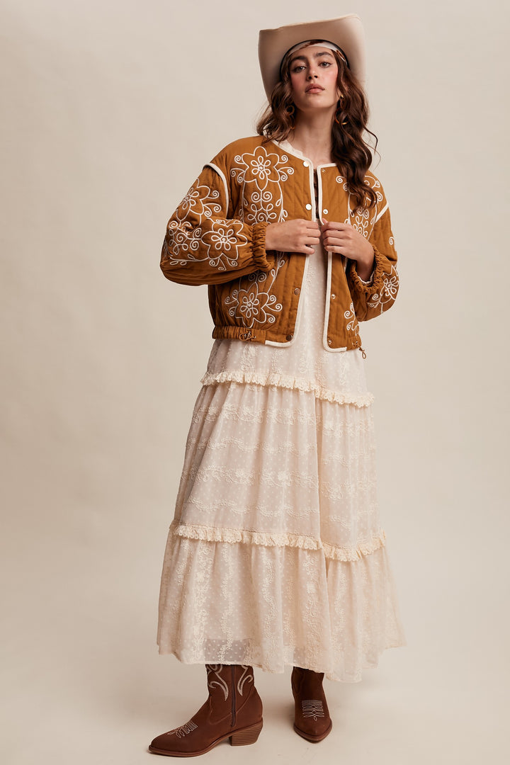 Woman wearing a embroidered jacket, white dress, and cowboy hat on a beige background