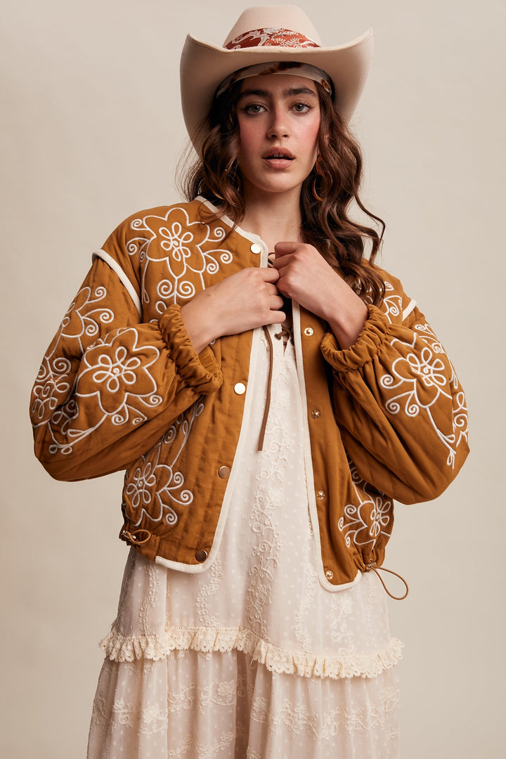 Woman wearing a brown embroidered jacket and white dress with a beige background