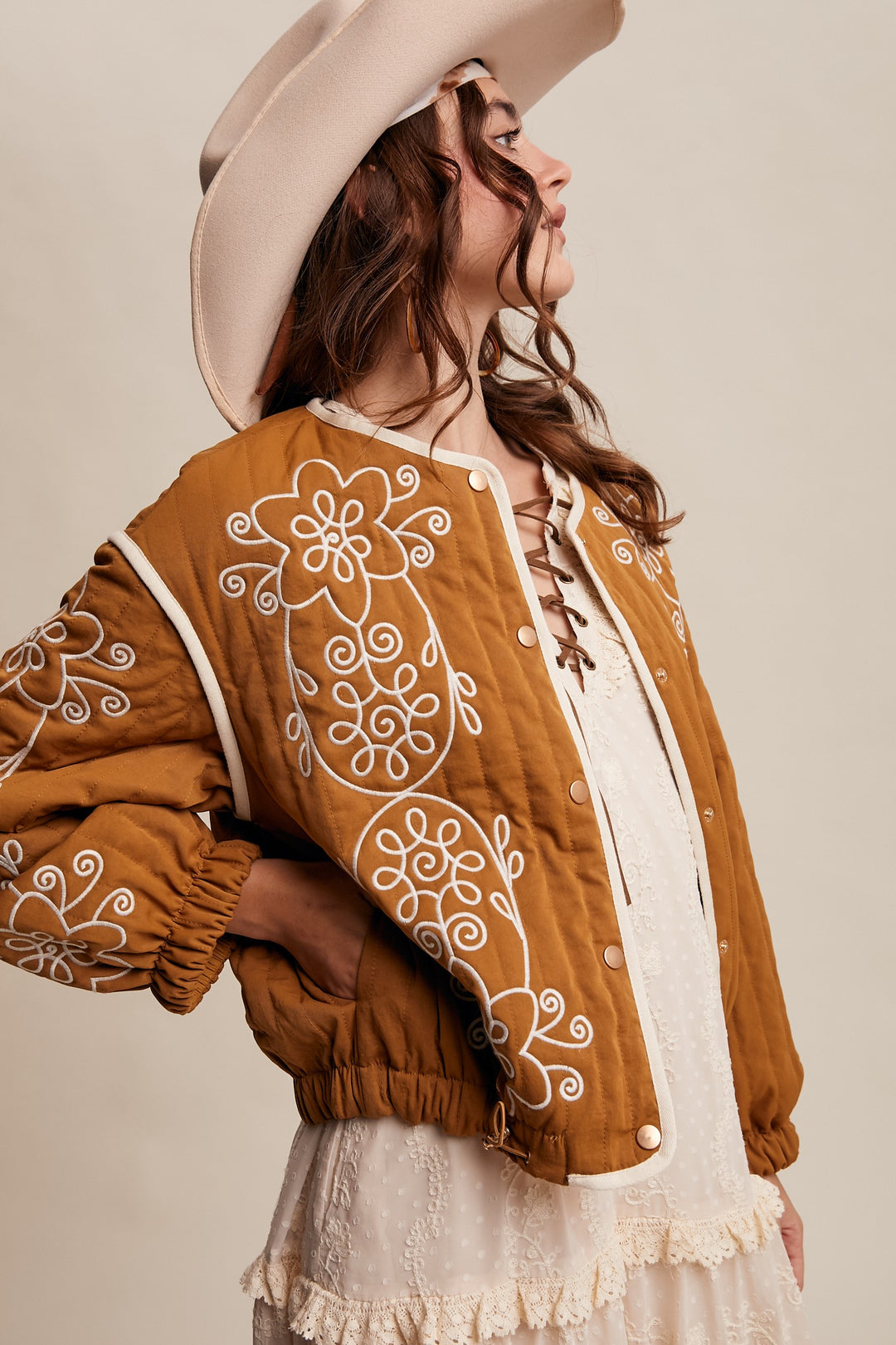 Woman wearing a brown embroidered jacket with a beige hat on a beige background