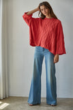 Woman wearing a red sweater and blue jeans against a plain background