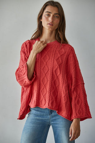 Woman wearing a red cable knit sweater and blue jeans against a gray background