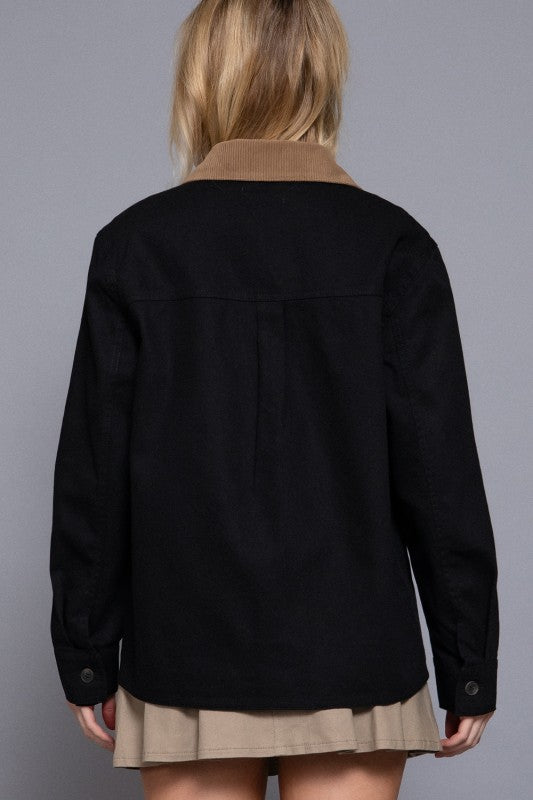 Person wearing a black jacket with a brown collar against a gray background