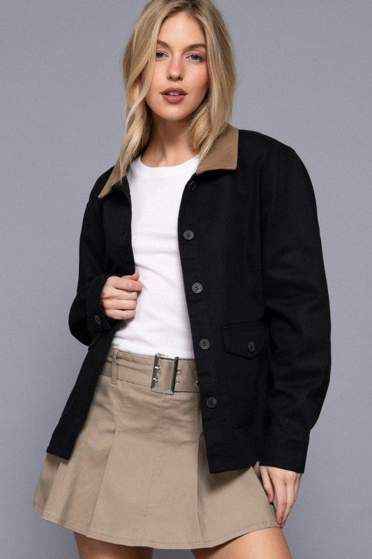 Woman wearing a black jacket over a white shirt and beige skirt on a gray background